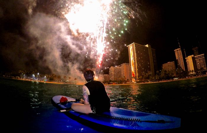 Nighttime paddle boarding under fireworks off Oahu