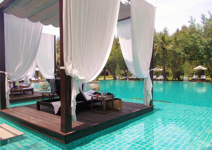 Individual cabanas around a large pool surrounded by greenery at The Sarojin Khal Lak