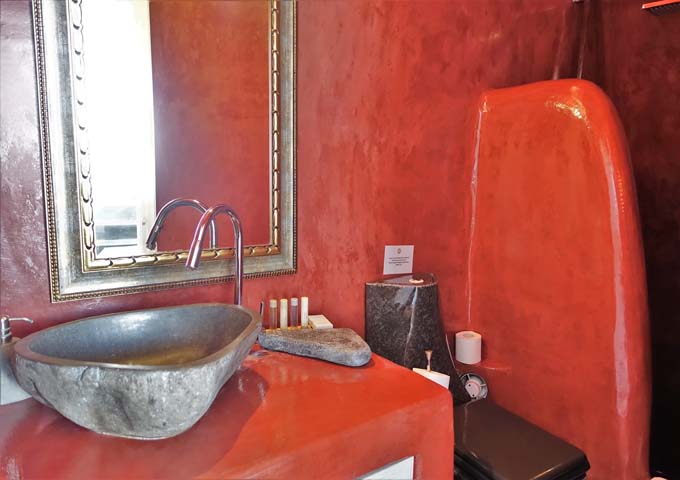 The bright red villa bathroom has a cave shower and rock sink.