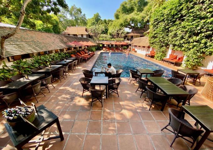 Red-tiled swimming pool patio lined by thatched-roof buildings and tables