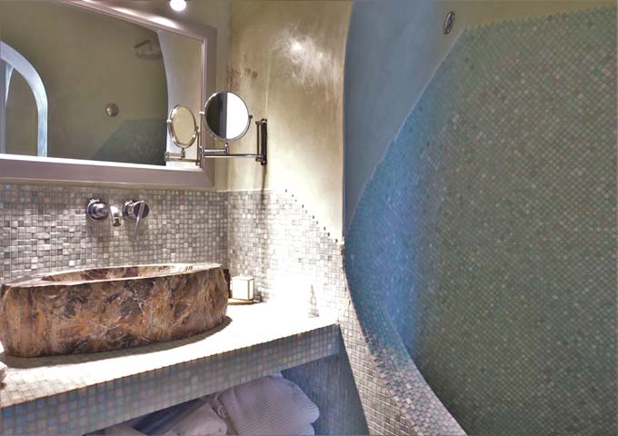 The bathroom has a cave-style open shower and a rock sink.