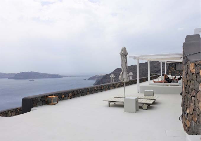 The pool deck has sun loungers and Bali beds, with views to Oia.