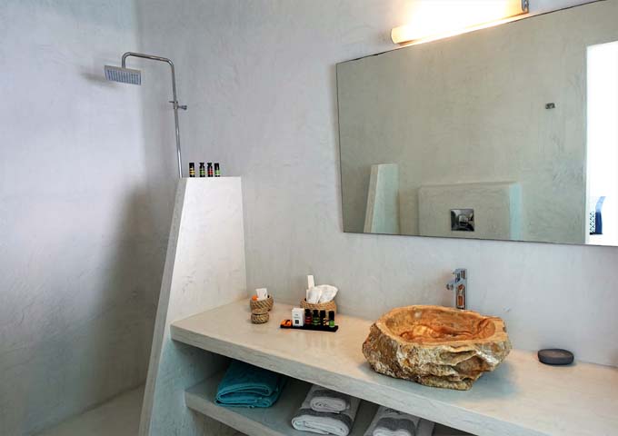The spacious bathroom has an open shower, rock sink, and large vanity area.