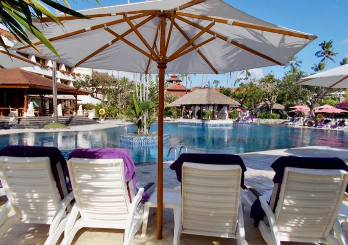 Lounge chairs with umbrellas surround the main pool.