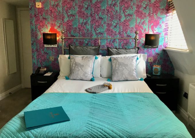 Hotel guest bed with vibrant wallpaper and a hot water bottle.