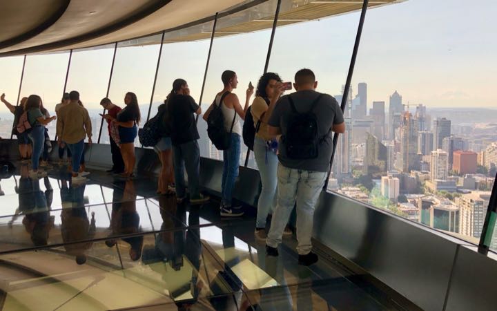 tourists looking at the view of Seattle from the Space Needle's inside observation area