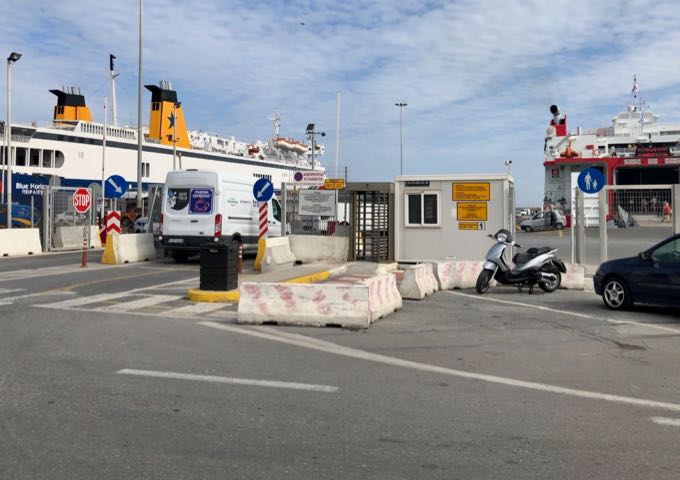 Port entrance with car and pedestrian gates, two ferries are docked in the background.
