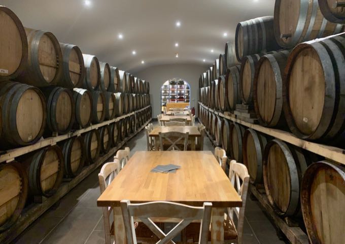 Tables for wine tasting set in the center of a long and narrow room lined with wine barrels.
