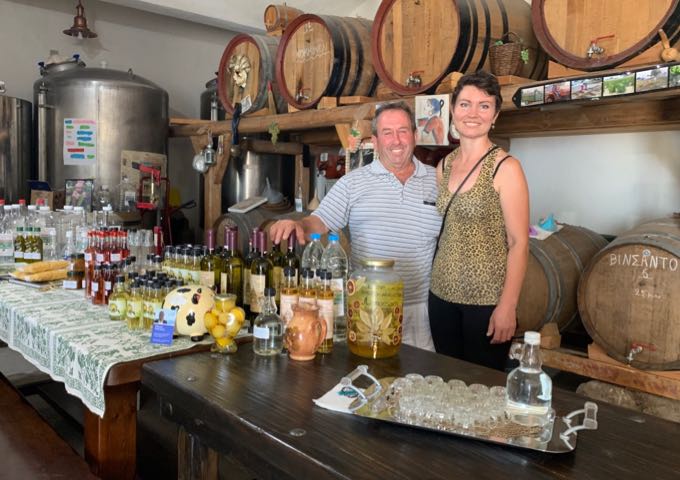 A couple stands next to a table full of wine bottles and homemade goods.