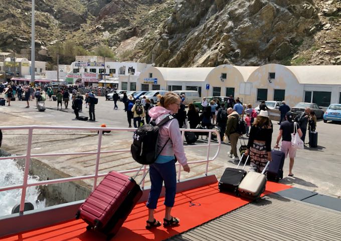 Passengers disembarking at Santorini ferry port with luggage. 