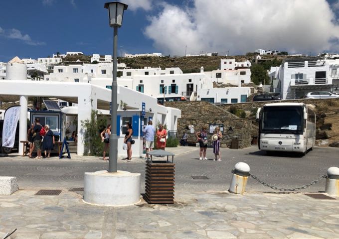 Bus station at Mykonos Old Port, with a bus and passengers waiting to purchase tickets.