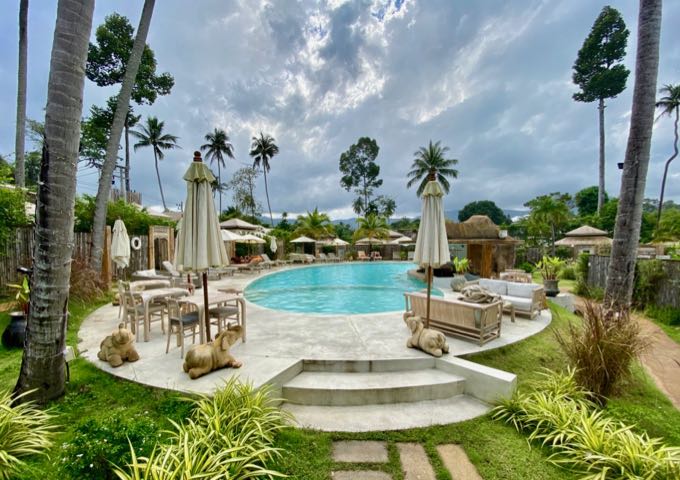 Small, elegant pool surrounded by loungers, umbrellas, palms, and elephant statues