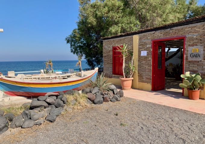 The stone exterior of Gaia Wines, with colorful painted wooden boats separating the parking area from the beach.