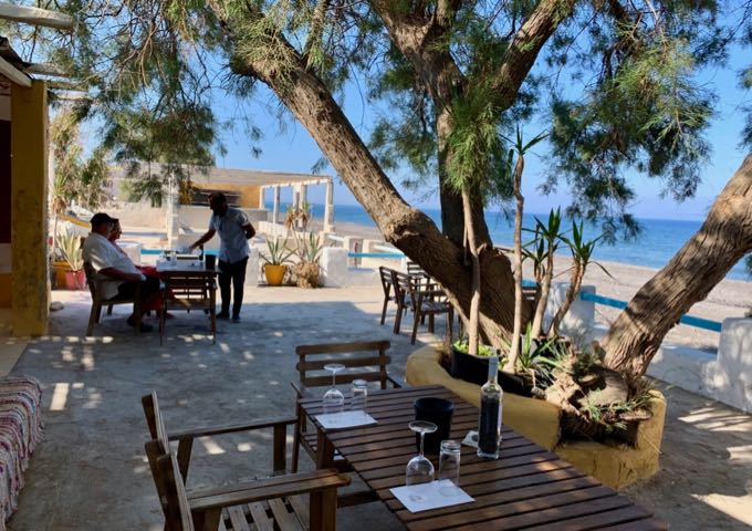 A man serves wine to a couple on a beachfront terrace of a winery on Santorini