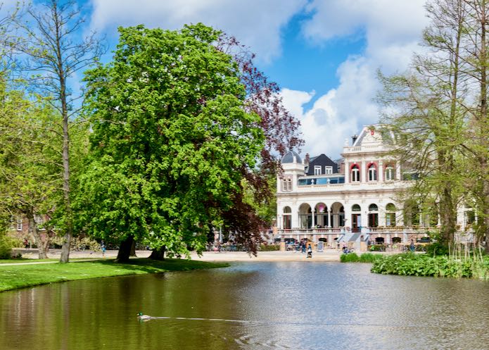 Park setting with a large pond, trees, and beautiful building