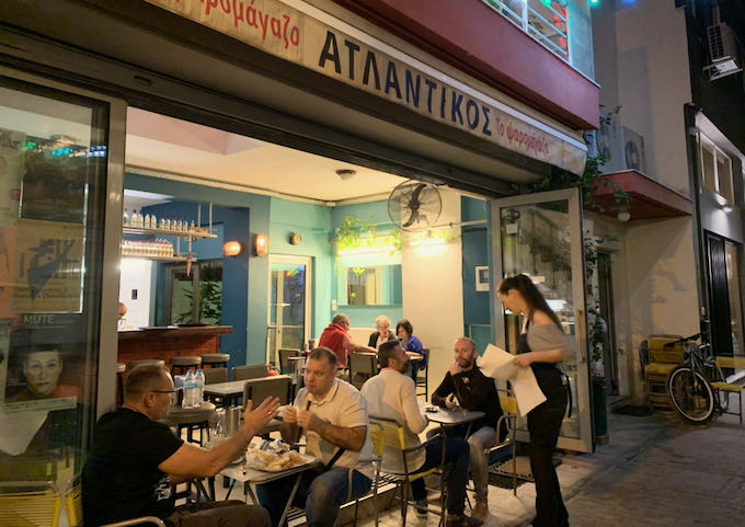 Waitress serving a sidewalk table at a Greek cafe after dusk