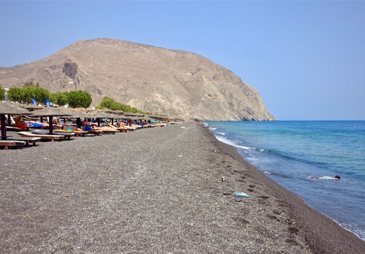 Beach loungers lined up on the black sand shore of Perissa on Santorini