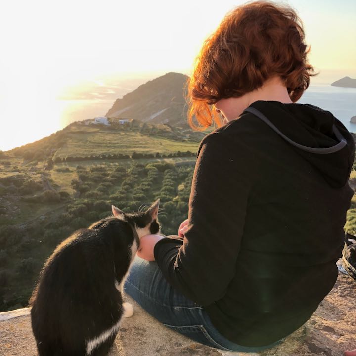A young girl pets a cat as she watches the sunset in Greece