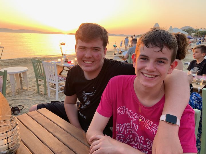 two teenage boys pose for a photo at a beachfront table