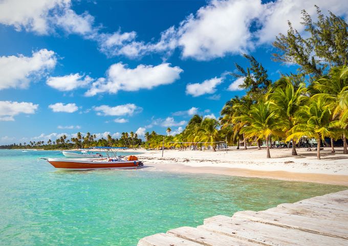 A boat is moored to a sandy beach lined with palm trees.