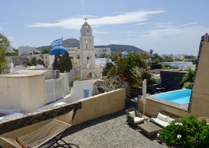 A cobblestone courtyard with hammock and private pool set against the backdrop of a traditional Greek church