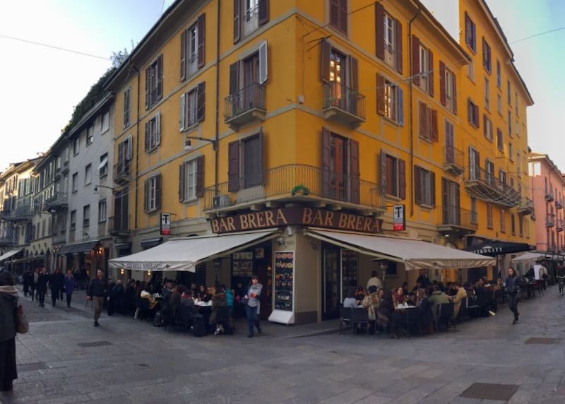 Mustard yellow colored corner bar with covered sidewalk seating on a street in Italy