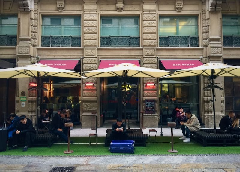 Patrons sit under umbrellas outside a bar in Milan