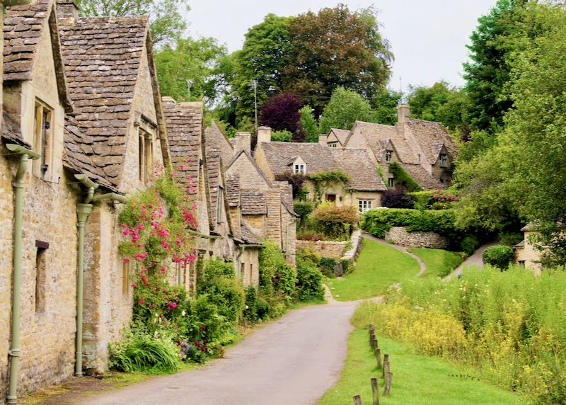 A row of stone English cottages with blooming flowers and rolling green lawns
