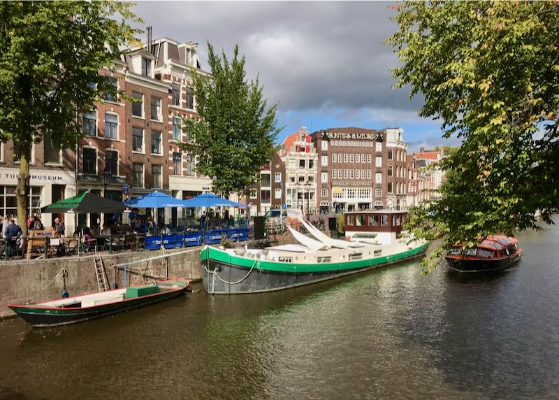 A tour boat passes by barges in the Amsterdam canals