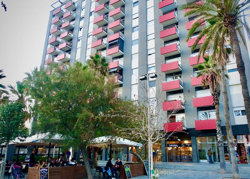 High-rise hotel with red balconies and a cafe in front