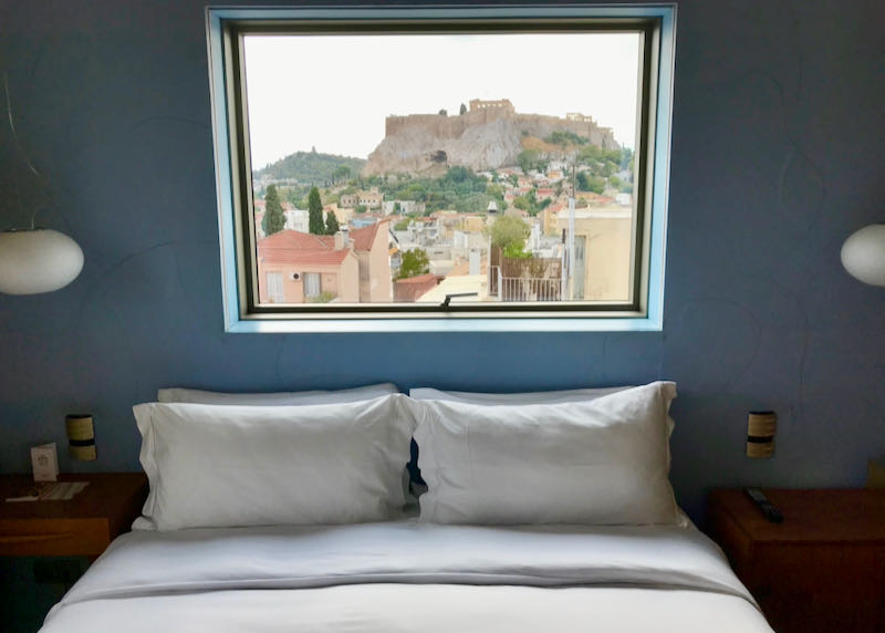 Hotel bed with a window above that has a view to the Acropolis