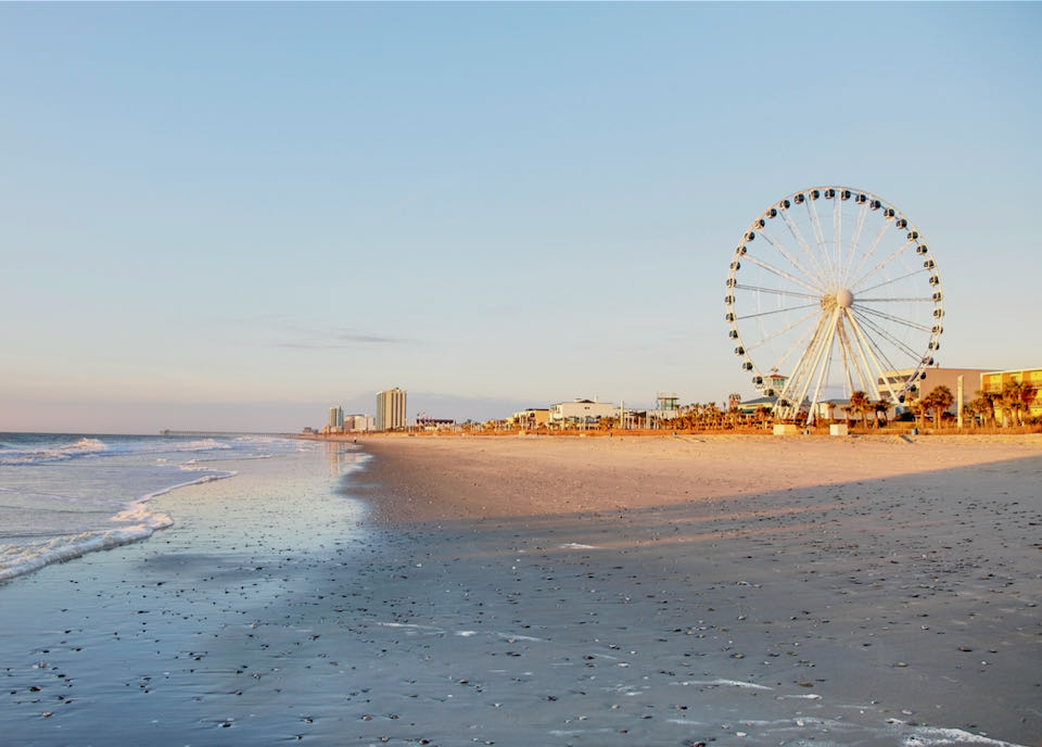 Sandy becah with many buildings and a ferris wheel in the distance