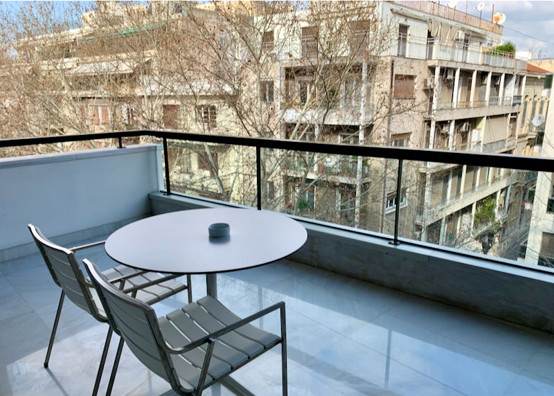 Balcony with a cafe table and chairs, overlooking plane trees and a city street