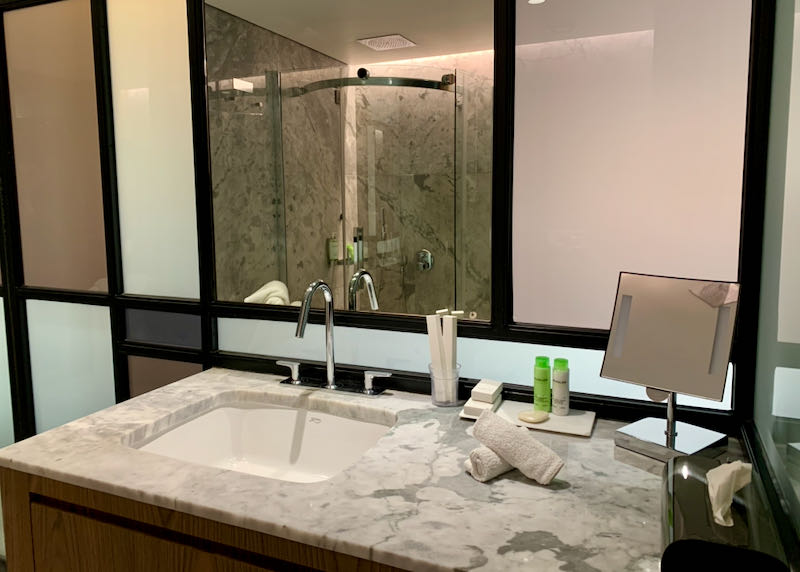 Marble vanity in a hotel bathroom, with mirror reflecting on a corner glass shower