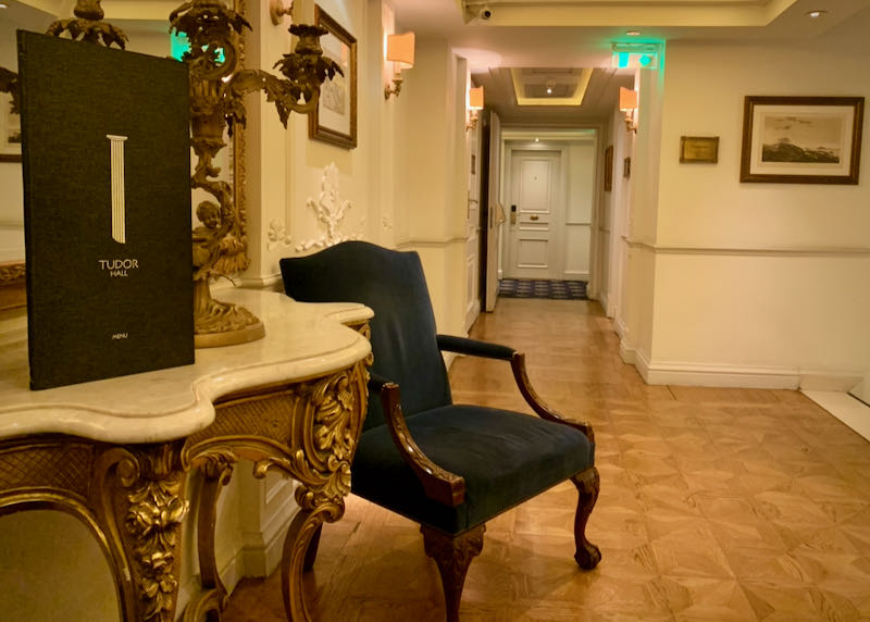 Entrance to a hotel restaurant with a menu propped up on a marble end table