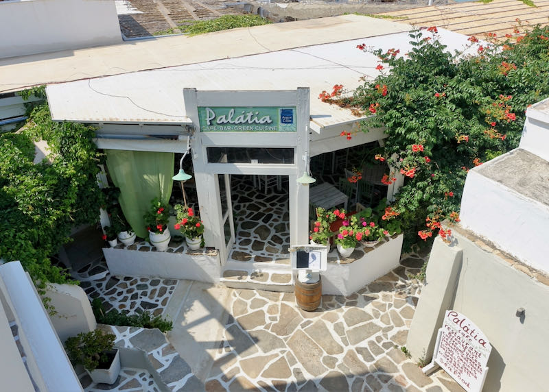 Entrance to a Greek restaurant with stone patio and many plants.