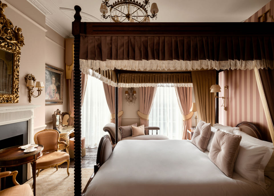 Four-poster canopied bed in a room with plush furnishings and draperies, and a fireplace
