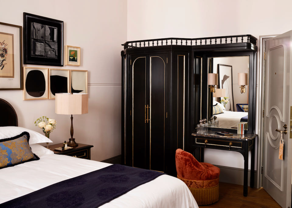 Hotel room with an antique armoire and a comfortable looking bed dressed in blush pink tones