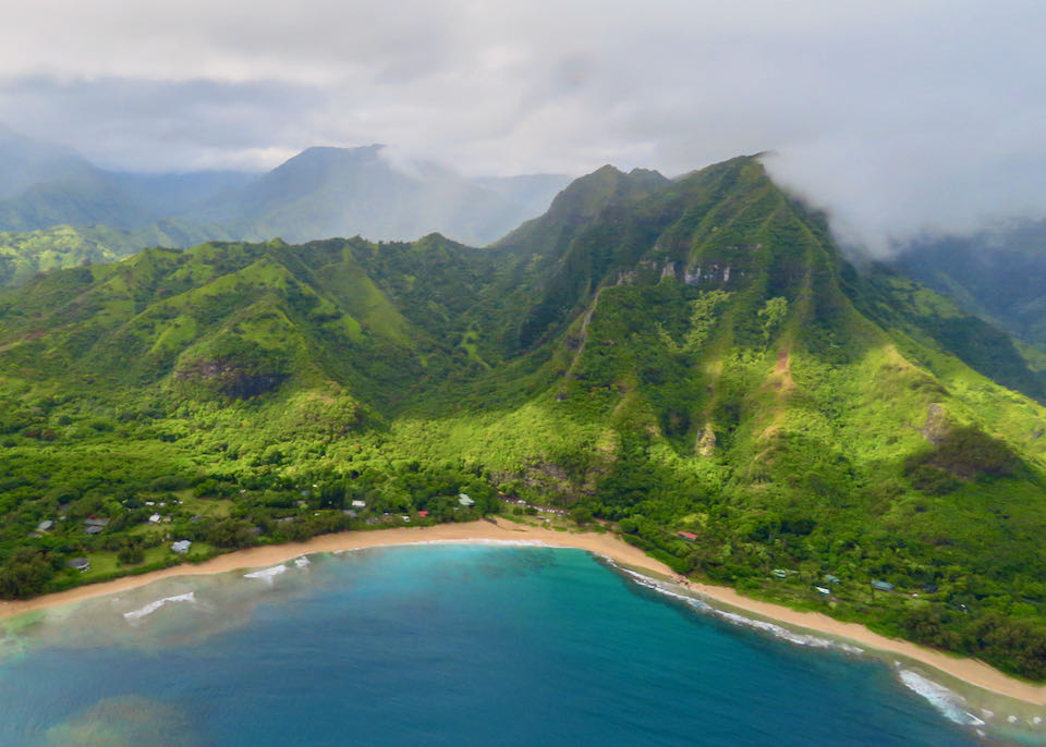 Aerial view of a golden sand beach backed by lush green mountains and mist