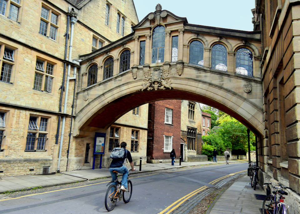 A cyclist rides beneath a passageway connecting two college buildings.
