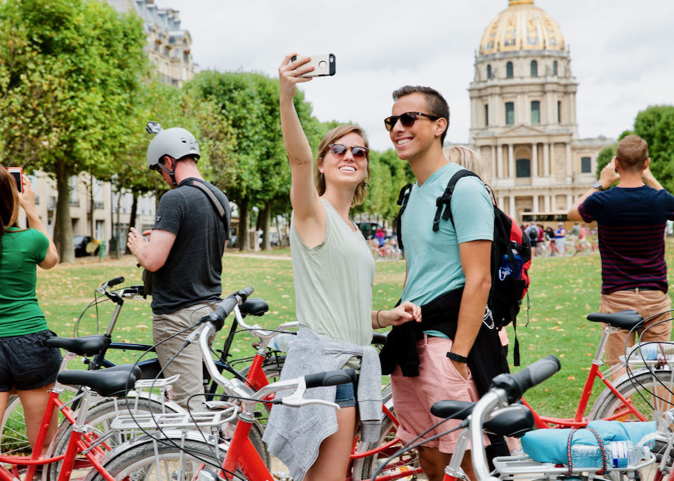 A couple take a selfie photo on bikes in front of a historic monument in Paris
