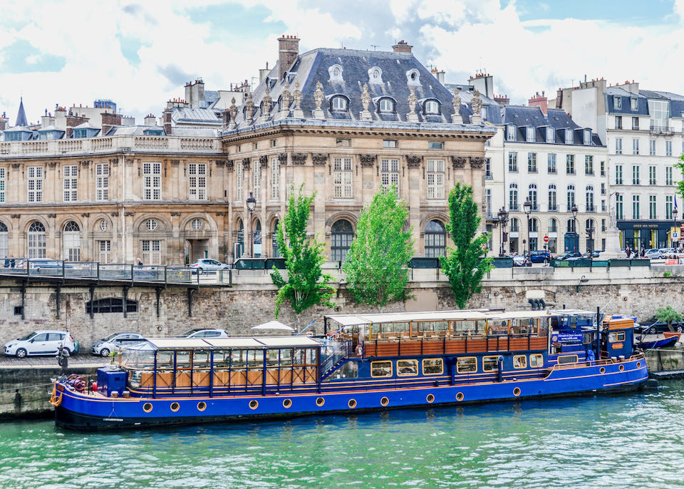 The blue-painted dinner boat, Le Calife, docked on the banks of the Seine, with elegant Haussmann-style buildings in the background
