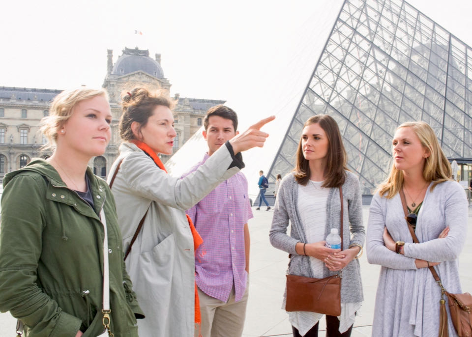 A woman points and explains to a group of tourists at the Louvre