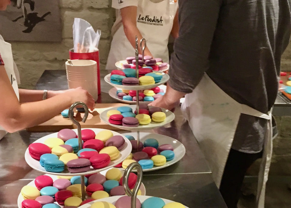 People in aprons stand around plates of colorful macarons.