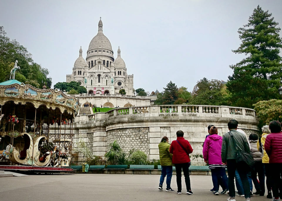 A group of tourists in parkas gaze up at the Scare Coeur basilica in Paris on a cloudy day
