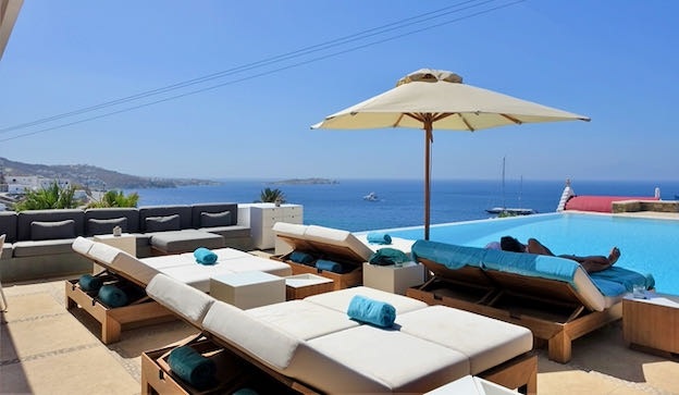Sun loungers surround a crystal blue infinity pool and overlook the Aegean Sea