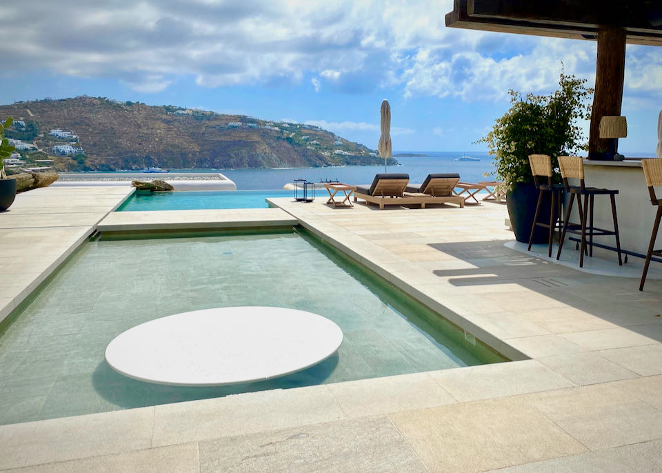 White marble pool deck with bar and infinity pool overlooking a bay in the Aegean Sea