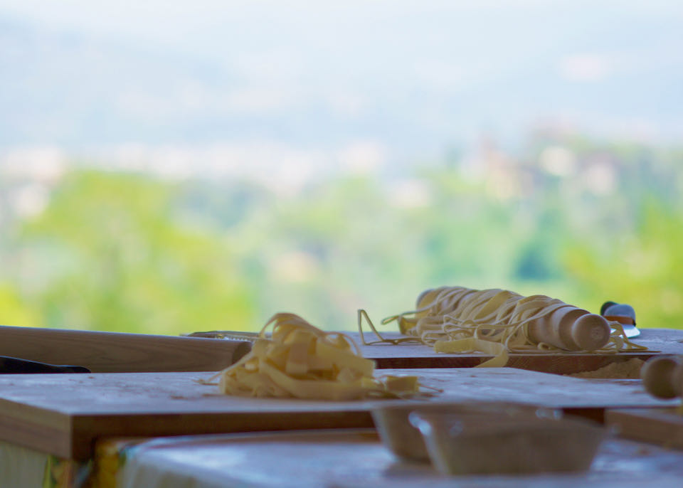A pile of freshly-cut pasta sits on a table in the outdoors, with a greenery backdrop