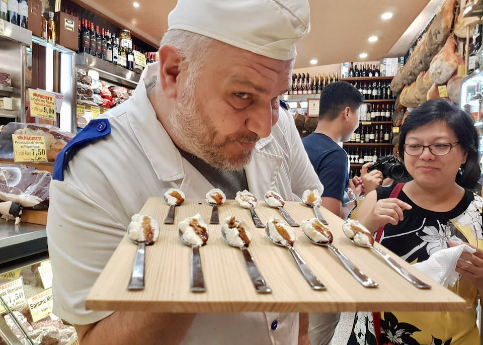 A man in a chef's hat tempts the viewer with a tray of ricotta and balsamic vinegar
