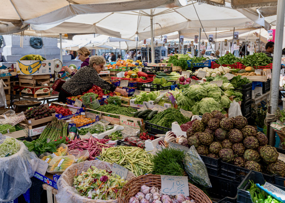 A woman picks produce from a colorful and bountiful farmers' market stall.